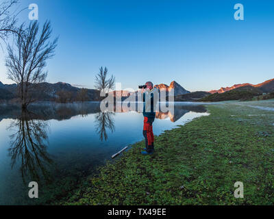 Spain, Asturias, Camposolillo, Cantabrian Mountains, senior man taking a photo at the seashore of Porma reservoir Stock Photo