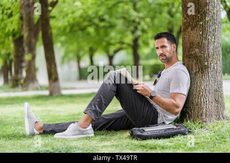 Man leaning against a tree in park reading newspaper Stock Photo