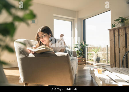 Relaxed young woman lying on couch reading a book Stock Photo