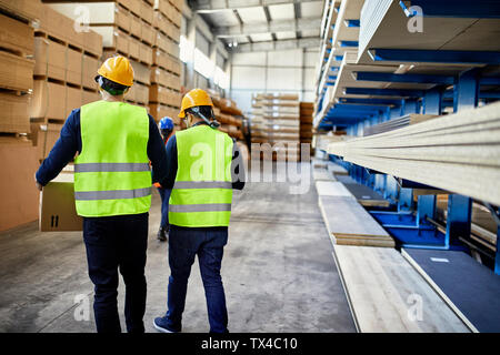 Rear view of two workers carrying boxes in factory warehouse Stock Photo