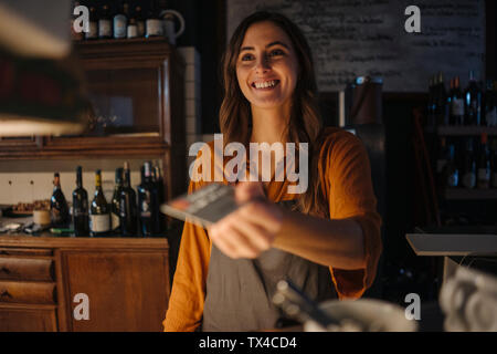 Smiling young woman at restaurant counter handing over credit card Stock Photo