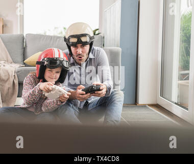 Young man and little girl wearing biker helmets, playing racing game with gaming consoles Stock Photo