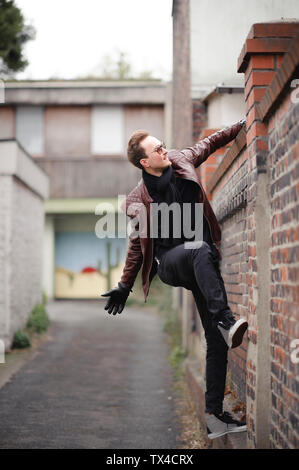 Young man climbing over brick wall Stock Photo