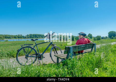 Germany, Zons, senior man with bicycle resting on a bench looking at view Stock Photo