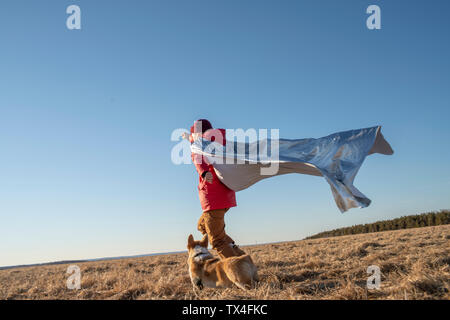 Boy dressed up as superhero running with dog in steppe landscape Stock Photo