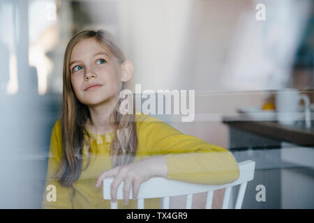 Portrait of a girl sitting on chair at home looking up Stock Photo