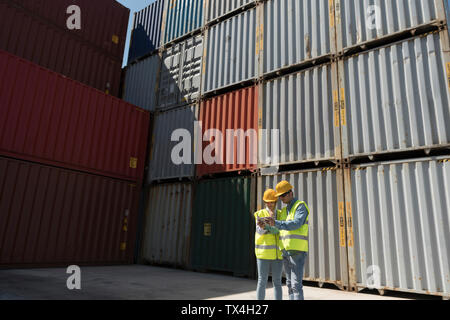 Workers using tablet in front of cargo containers on industrial site Stock Photo