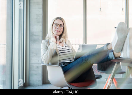 Relaxed businesswoman using laptop in office with feet up Stock Photo