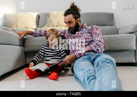 Father and little daughter sitting in the floor in the living room reading a book together Stock Photo