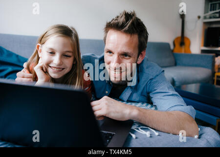 Happy father and daughter lying on couch at home using laptop Stock Photo