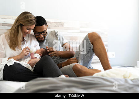 Happy father and mother bottle-feeding their newborn baby in bed Stock Photo