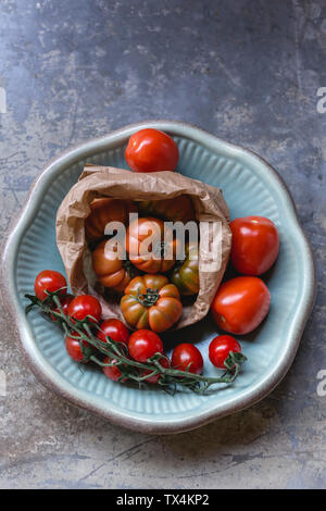 Sardinian beef tomatoes in paper bag, risp of mini plum tomatoes and Roma tomatoes on plate Stock Photo