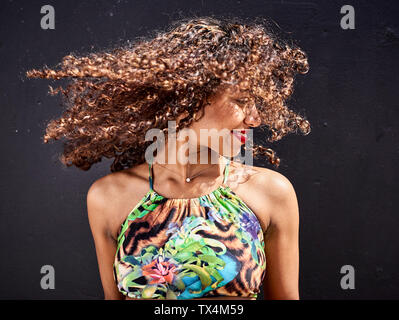 Smiling young woman tossing her curly hair in front of dark background