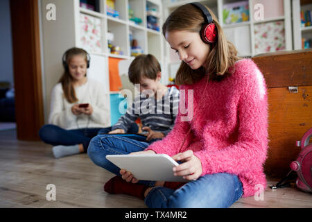 Siblings playing at home with their digital tablets, sitting on ground Stock Photo