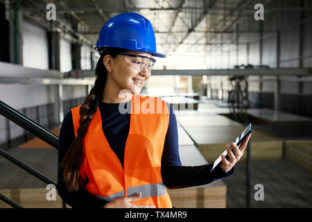 Smiling female worker using tablet in factory warehouse Stock Photo