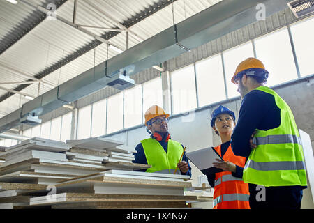 Two men and woman in reflective vests discussing in factory Stock Photo