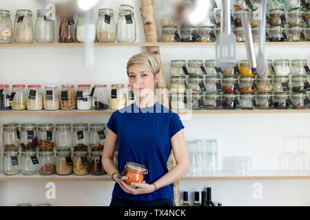 Portrait of woman holding jar in front of spice shelf in kitchen