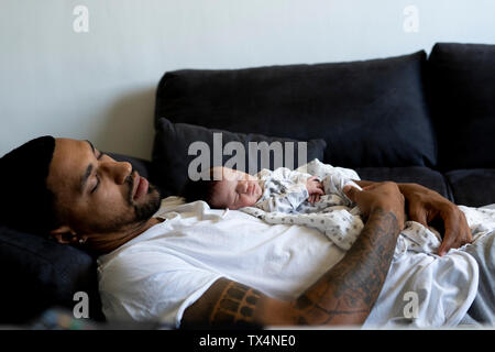 Father with newborn baby sleeping on couch