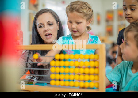 Pre-school teacher with children in kindergarten using abacus Stock Photo