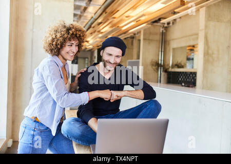 Happy man and woman with laptop fist bumping in modern office Stock Photo