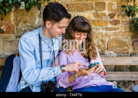 Young couple on a city break, sitting on a bench, using smartphone Stock Photo
