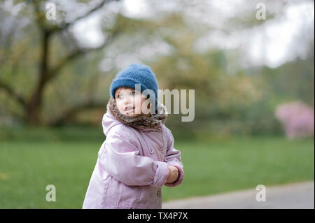Portrait of little girl in a park wearing blue hat and pink coat Stock Photo