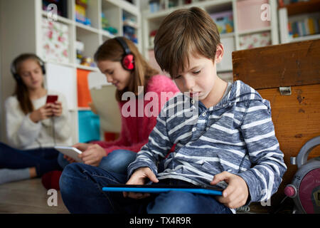 Siblings playing at home with their digital tablets, sitting on ground Stock Photo