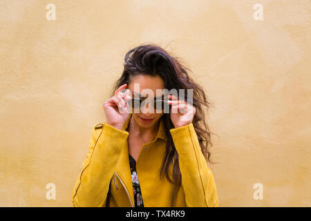 Portrait of young woman wearing yellow leather jacket and sun glasses Stock Photo