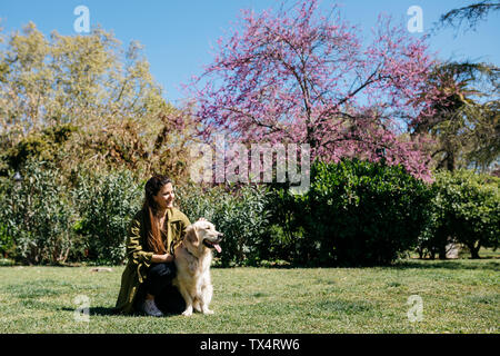 Happy woman stroking her Labrador Retriever on meadow in city park Stock Photo