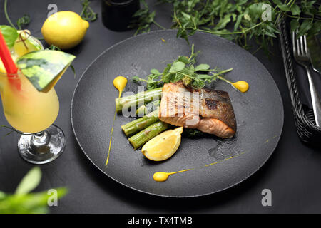 Baked salmon fillet with lemon sauce served on green asparagus. An elegant exquisite dish. Stock Photo