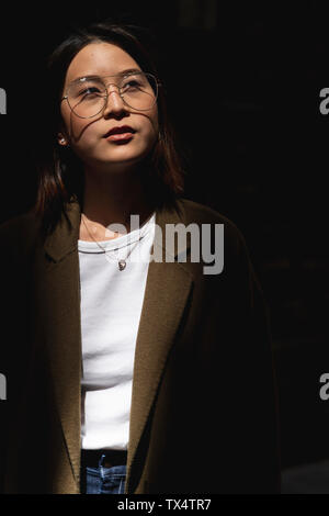 Portrait of young woman wearing glasses in sunlight looking around Stock Photo
