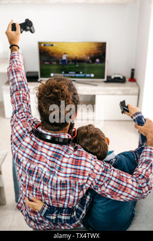 Back view of happy father and son sitting together on the couch playing computer game Stock Photo
