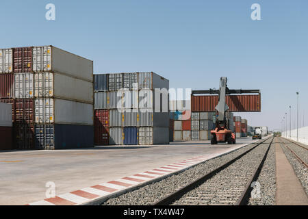 Crane lifting cargo container near railway tracks on industrial site ...