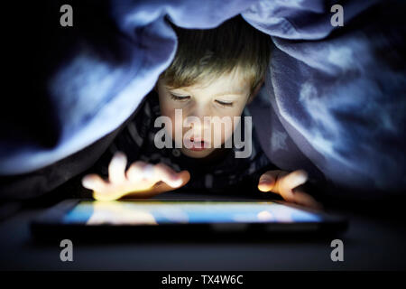 Little boy playing secretly with his digital tablet, hidden uunder blanket Stock Photo