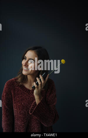 Smiling young woman using flower as antenna for cell phone Stock Photo