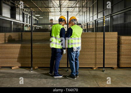 Rear view of workers standing at grid in factory Stock Photo