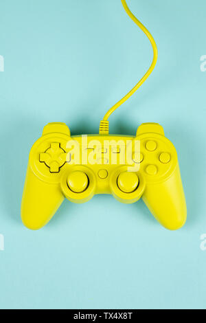 a yellow painted video game controller on a plain turquoise background. Minimal color still life photography Stock Photo