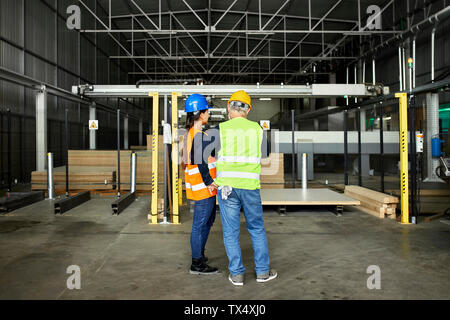 Rear view of male and female worker standing in factory workshop Stock Photo