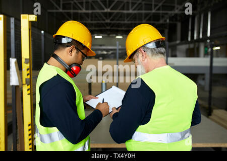 Two men signing document in factory warehouse Stock Photo