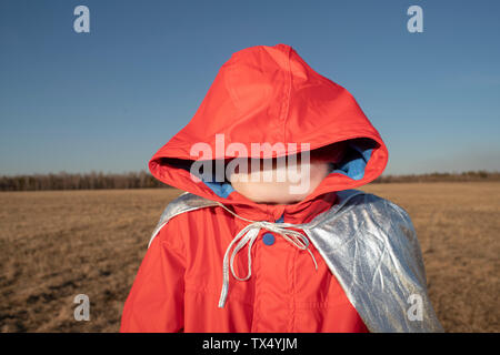 Boy dressed up as superhero in steppe landscape hiding his face in hood of his jacket Stock Photo