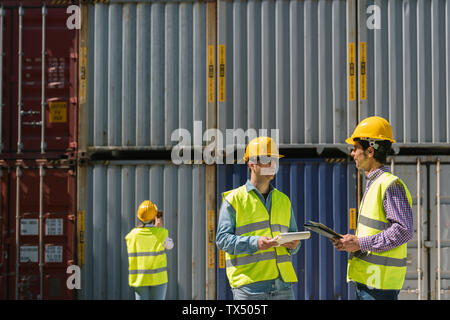 Workers talking near stack of cargo containers on industrial site Stock Photo