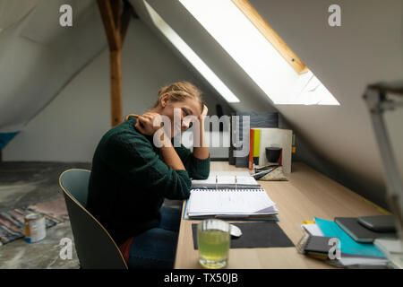 Young woman sitting at desk in attic studying folder Stock Photo