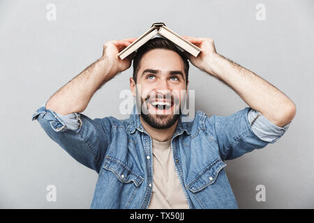 Excited cheerful man wearing shirt isolated over gray background, holding open book on his head Stock Photo