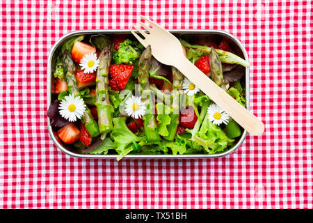 Lunchbox with green salad, green asparagus, strawberries and daisies Stock Photo