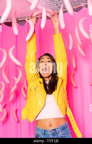 Young woman screaming at an indoor theme park with dangling pink bananas Stock Photo