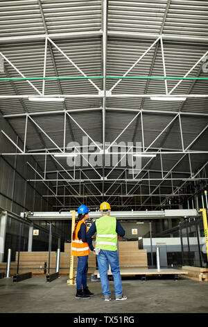 Rear view of male and female worker standing in factory workshop Stock Photo