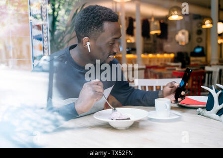 Smiling young man with earphones and smartphone behind windowpane in a restaurant Stock Photo