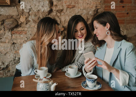Three young women looking at cell phone in a cafe Stock Photo