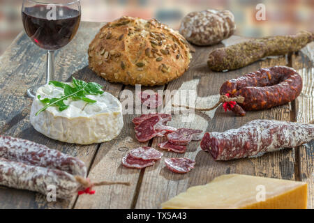 French snacks with wine - various types of cheeses, bread , dry saussages, charcuterie, red vine on a gray background. Top view. Stock Photo