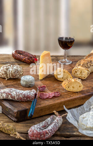 French snacks with wine - various types of cheeses, bread , dry saussages, charcuterie, red vine on a gray background. Stock Photo
